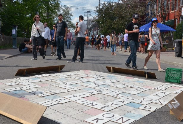 People are walking towards the camera, down the street, but between them and the camera is a giant scrabble game that is now finished
