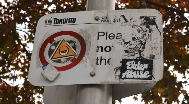 A city of Toronto sign that has had four stickers attached to it.  
