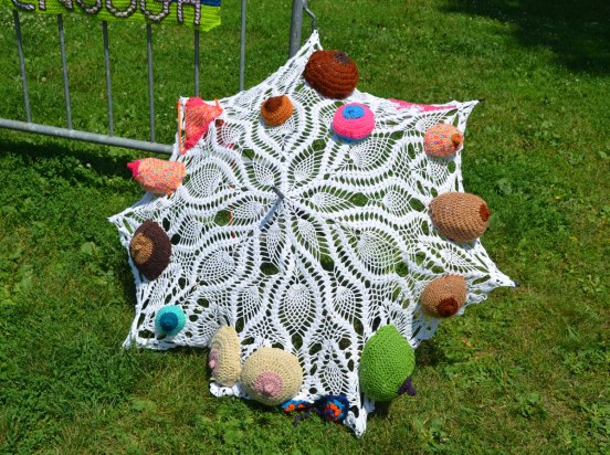 A lacy umbrella decorated with crocheted 3D breasts in different colours, probably life sized. 