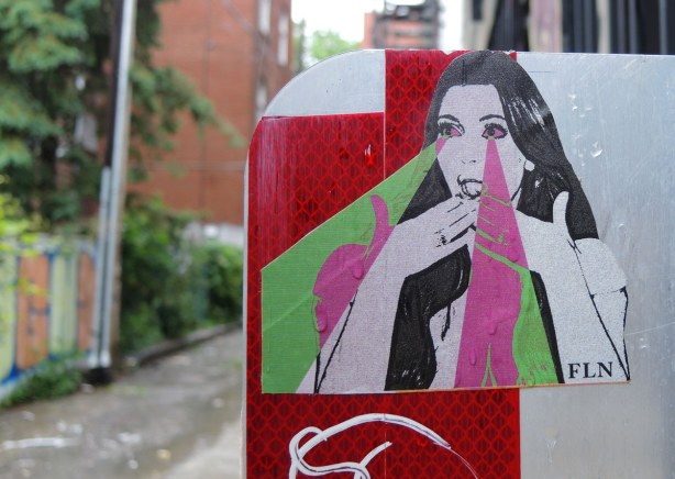 little people graffiti, sticker of a woman holding her hands over her mouth.  rays of green and pink are coming from her eyes.  FLN, or futur lasor now, is the name on the bottom right corner of the sticker 