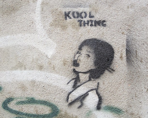 little people graffiti, black line drawing on grey concrete of a girls' head in profile.  The eords Kool Thing are written abover her head. 