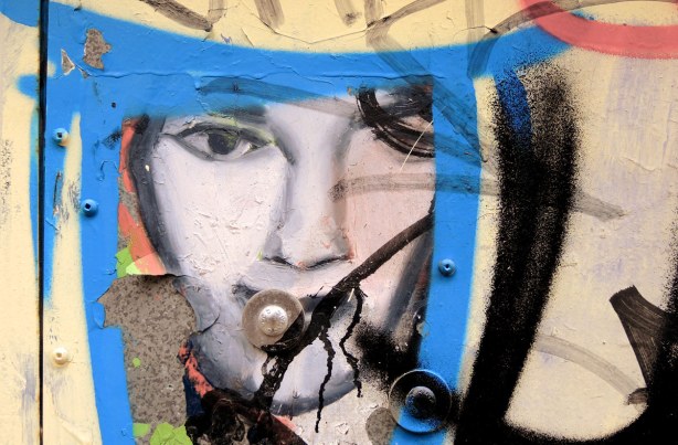 little people graffiti, sticker of a woman's face.  A blue triangle has been painted around it