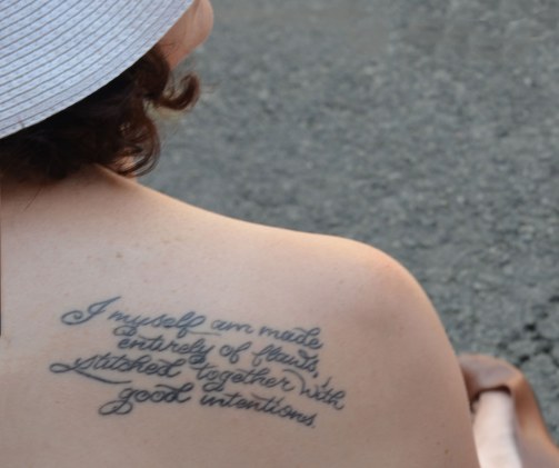 A woman's bare shoulders exposing a tattoo that says I myself am made entirely of flaws stitched together with good intentions