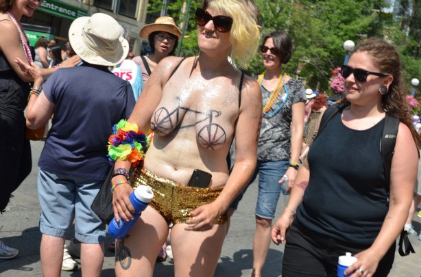 A woman wearing gold shiney shorts with her cellphone tucked into the top of them.  SHe is barebrested but with a large black bicycle drawn across them. 