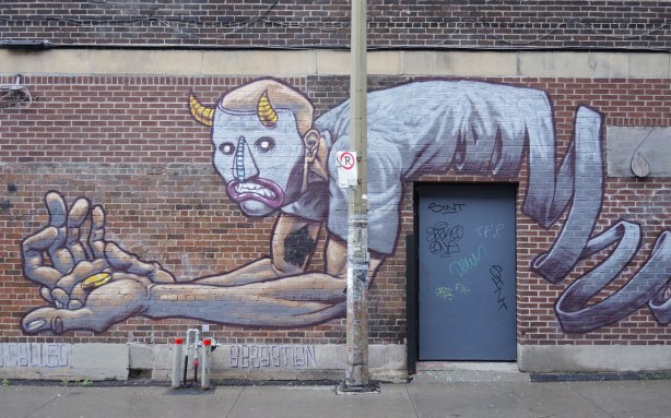 mural of a man lying over the top of a real door.  He is on his elbows on one side of the door.  He doesn't have legs though,  instead a long coiled something is where his legs should be.  