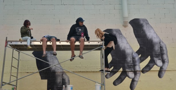 Street art of large hands that have been printed on paper and then pasted to a wall.  
