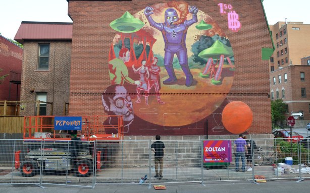a large mural on the side of a red brick wall in Montreal.  A purple robot like monster is the central figure in the mural by the artist Zoltan