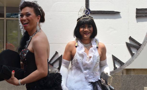 Two women, or men dressed as women, one in black and one in white. The one in white has a large black & white clockface behind her