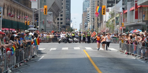 crowds are behind barricades along the streets, policemen on motorcycles are waiting at the end of the street. parade hasn't started yet
