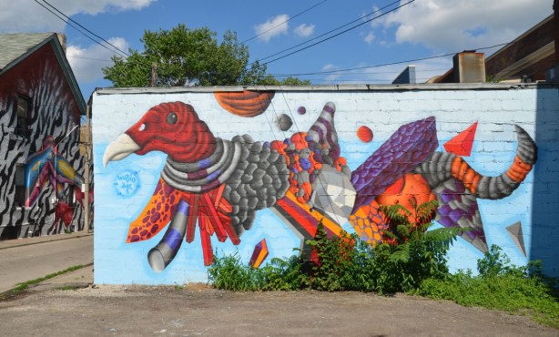 large mural street art piece painted on the side of a one storey building of a beaked creature with wings