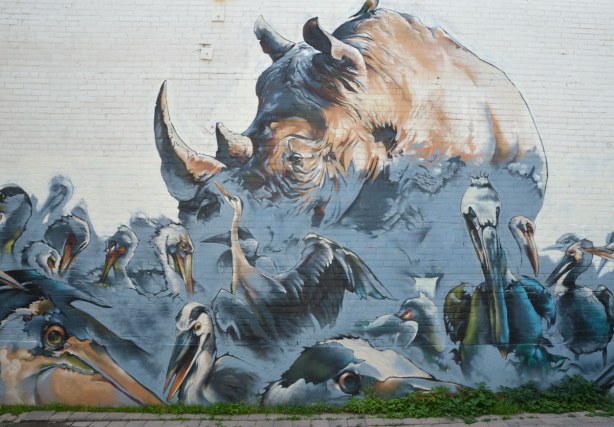 large mural on the side of two storey building of a rhino surrounded by large birds