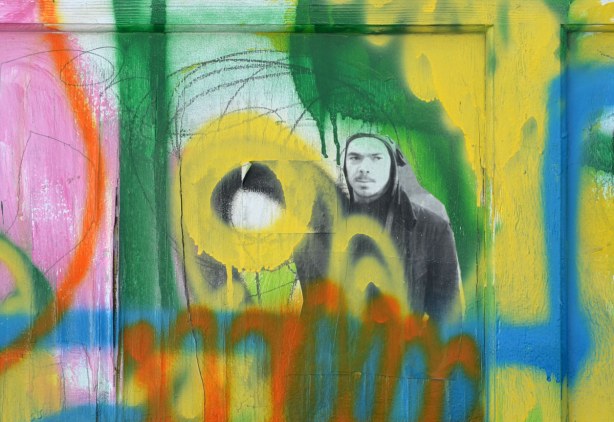 A small black & white & grey face made on paper, surrounded by  green , yellow, blue & oranges squiggly lines