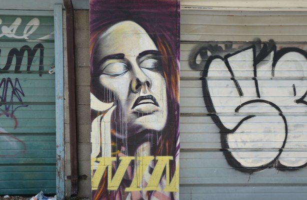 A street art painting of a woman's face.  Her eyes are closed and her head is tilted upwards