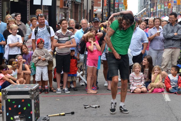 A street performer is twisting the upper part of his body in order to fit it through a tennis racquet.
