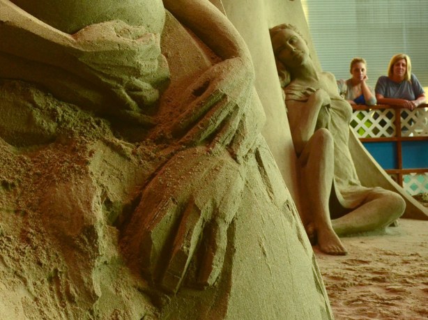 Details of a sand sculpture (hands) with another sculpture behind (of a woman)
