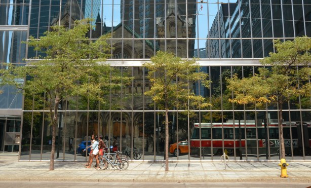 Reflections in the building across the street, some women are walking by with their bicycles, a street car is just coming into view. 