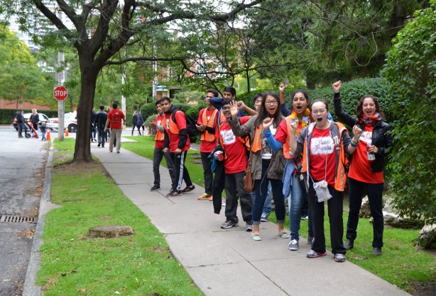 people at the AIDS walk in Toronto.  A group of volunteers is cheering on those who have walked so far.  They are standing on the sidewalk. 