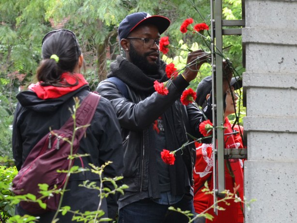 people at the AIDS walk in Toronto.  A man is putting a red carnation on the AIDS Memorial in Toronto.  Quite a few carnations are already there. 