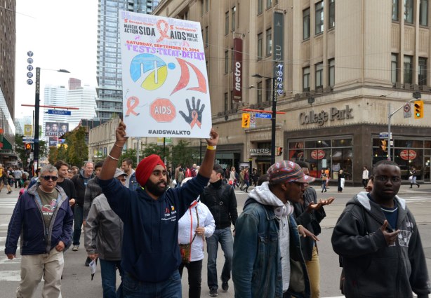 people at the AIDS walk in Toronto.  A Sikh man wearing a red turban is holding up a poster about treating and defeating AIDS. 