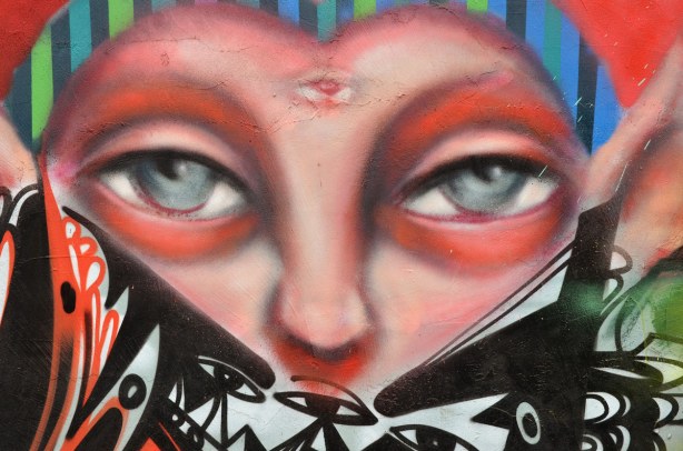 Colourful graffiti in a Kensington lane. Close up of a pair of grey eyes. Bottom part of face is obscured, including her cheeks.