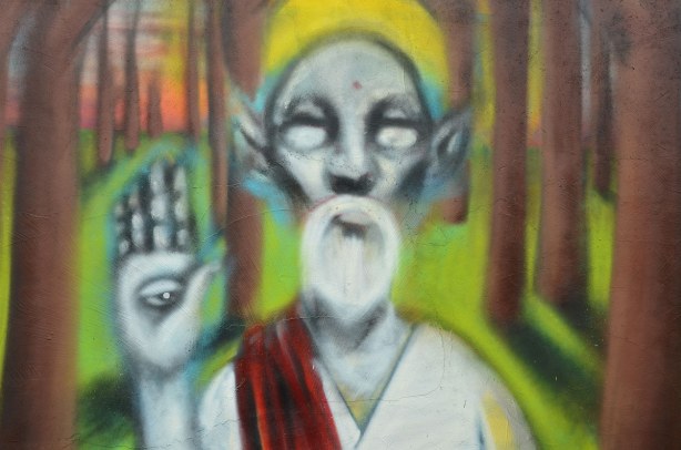 Colourful graffiti in a Kensington lane, an oldered bearded man with yellow hat (or turban?) is holding up his hand to show the eye that is on his palm.