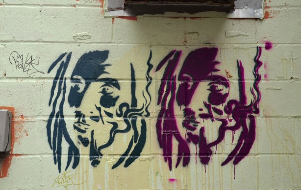 Colourful graffiti in a Kensington lane stencils of heads, one dark blue and one purple.