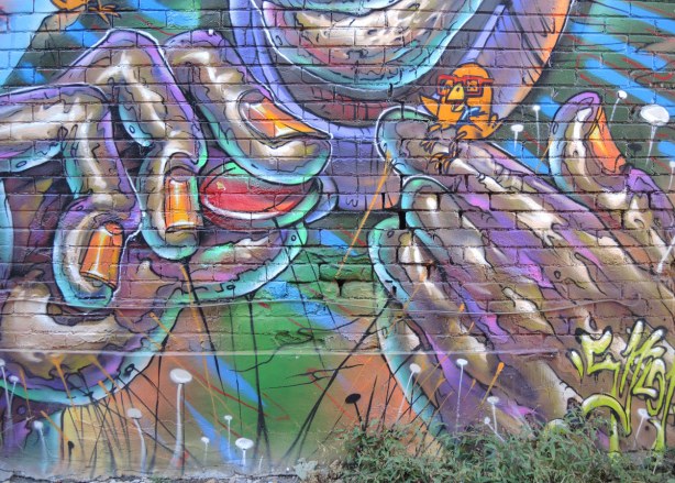 part of a large mural on the side of a 2 storey building, a small uber chicken is being held between two fingers of a very large pair of hands