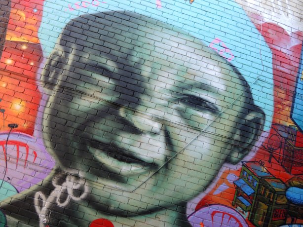 part of a large mural, a picture of a smiling small boy wearing a light blue cap. It is very large. 