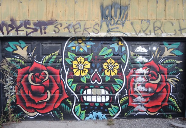 a garage door that has been painted with two very large red roses on either side of a painting of a skull with lots of flowery motifs in it. 