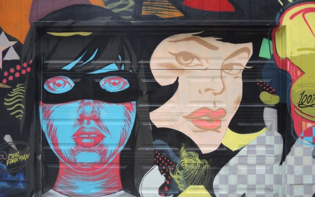 Street art piece of two large women's heads.  One is blue and she's wearing a black mask.  