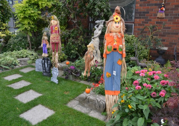 A front yard has autumn decorations - straw men in funny hats and patchwork clothes.