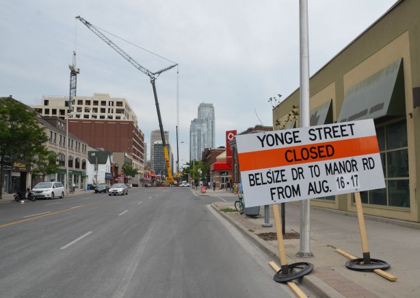 Yonge street is closed by a large crane that is parked in the middle of the street. 