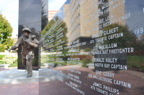 A short wall of black rock has the names of fallen firefighters carved in it.  In the background is the statue of the firefighter and young boy.