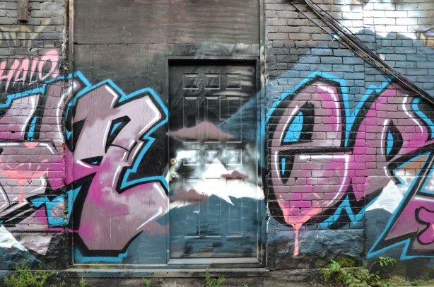 large pink graffiti tag letters on either side of a black door in an alley
