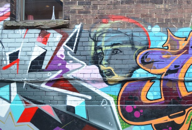 graffiti face between two colourful tags. Part of a window is the picture and there is a small Eiffel Tower on the window sill.