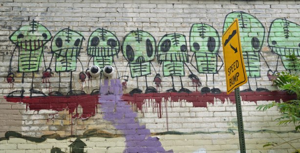 a line of graffiti little green guys that look sort of like aliens with stick arms and legs and big black eyes.