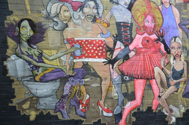 detail from mural - a bearded man in a pink dress, a woman in purple and two people sharing the same red & white polka dot dress