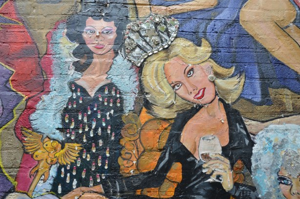 detail of mural - two women, one in black low cut dress and silver sparkly crown and the other in a bejeweled black dress and white fur boa. 