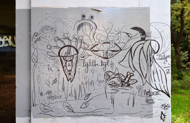 graffiti under a bridge - black and white line drawings of leaves and other biological looking creatures or things.  The words 'yellow ochre' and 'lylith lyl' also appear'