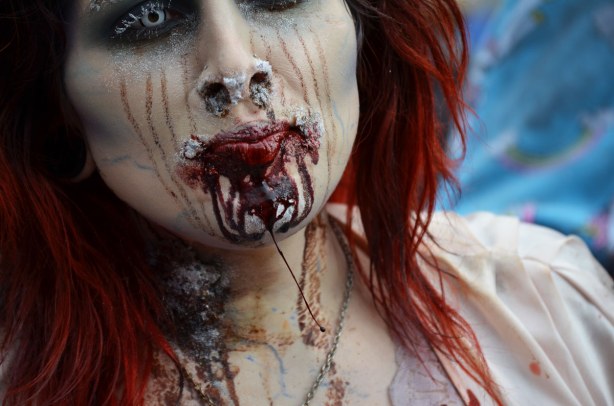 zombie woman with scratch marks on face and blood dripping down her chin.  Close up of just her head and shoulders.  Long red hair. 
