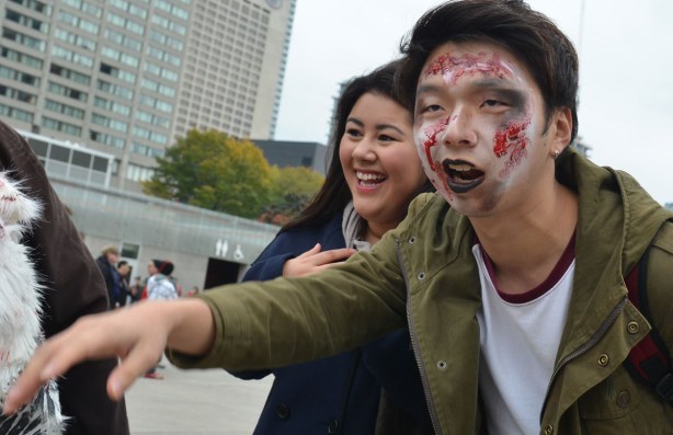 zombie from Toronto zombie walk, woman giggling as she poses beside a young man with his face made up to look like a zombie