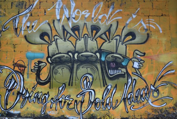 Street art in Graffiti Alley, a poser mural with 3 olive green bunnies.  The words, The World is Dying for Bold Ideas are written around the bunnies.  One bunny has a paint roller and another has a can of spray paint. 