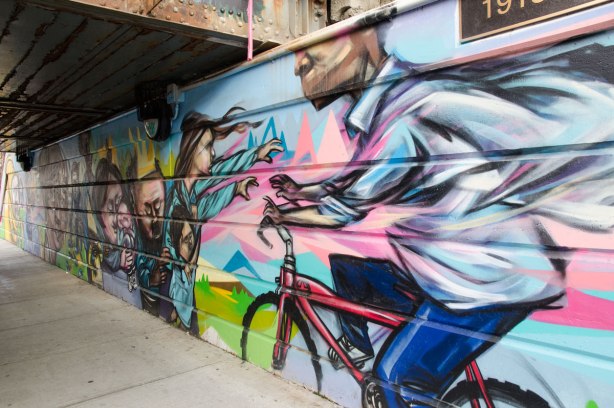 part of a mural beside the walkway under a railway bridge - a man on a red bike who is cycling towards a woman with outstretched arms