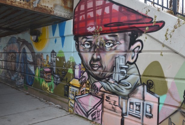 part of a mural beside the walkway under a railway bridge - a man with a red baseball cap on backwards