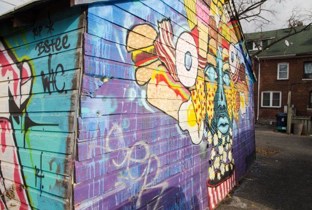 street art mural of a face in blue, yellow and red that is surrounded with stylized food, especially candy and popcorn. The neck is an iconic red and white striped popcorn container. viewed from the side on quite an angle