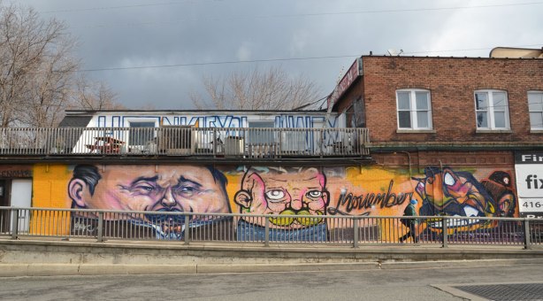 looking across the street to a mural to commemorate Movember. Two large men's faces, both sporting moustaches beside the word Movember written in cursive.