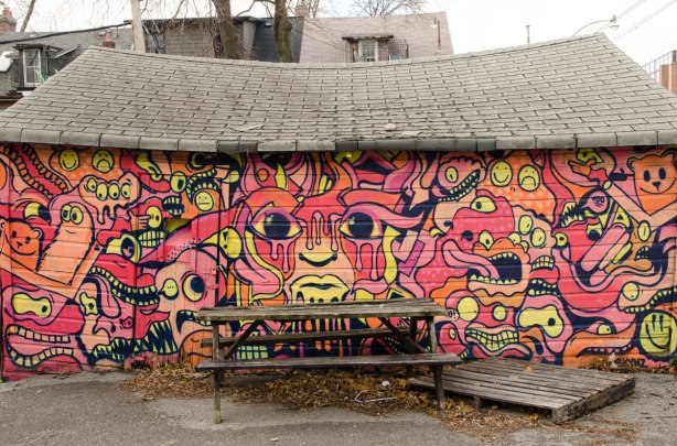 A wood picnic table is in front of a street art mural on the side of a garage door