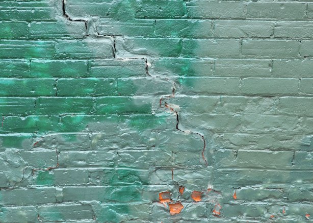 A brick wall painted in two shades of shiney green paint.  There is a large crack running diagonally across the wall. 