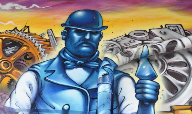 Paintings on the large T shaped concrete supports of the overpass, a man portrayed in blue tones, wearing an old fashioned hard hat and holding a trowel.  