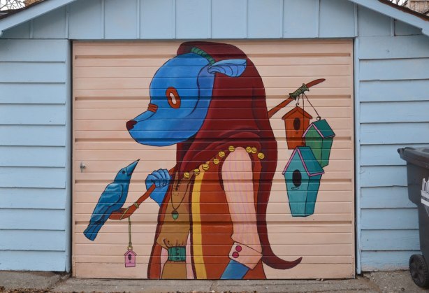 a blue animal like creature is carrying a stick over his shoulder. three wood bir houses are at the back of the stick. A blue bird is sitting in front on the stick, and looking at the creature.